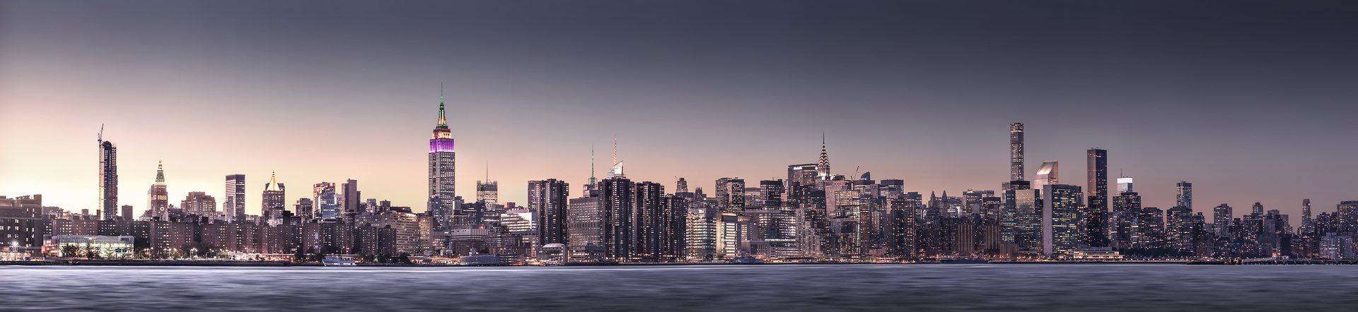 A panorama of a big city at night with lots of skyscrapers across a waterfront